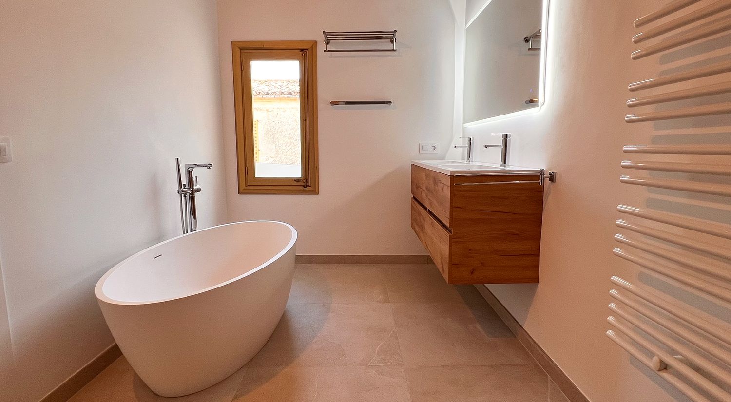 Modern bathroom interior with freestanding oval bathtub, wooden vanity, and natural light from window.