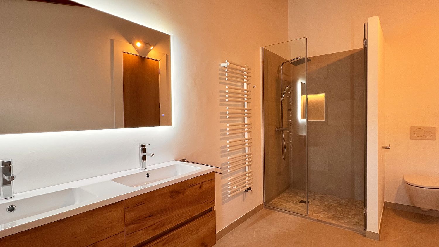 Modern bathroom featuring wooden vanity, double sinks and glass shower enclosure.
