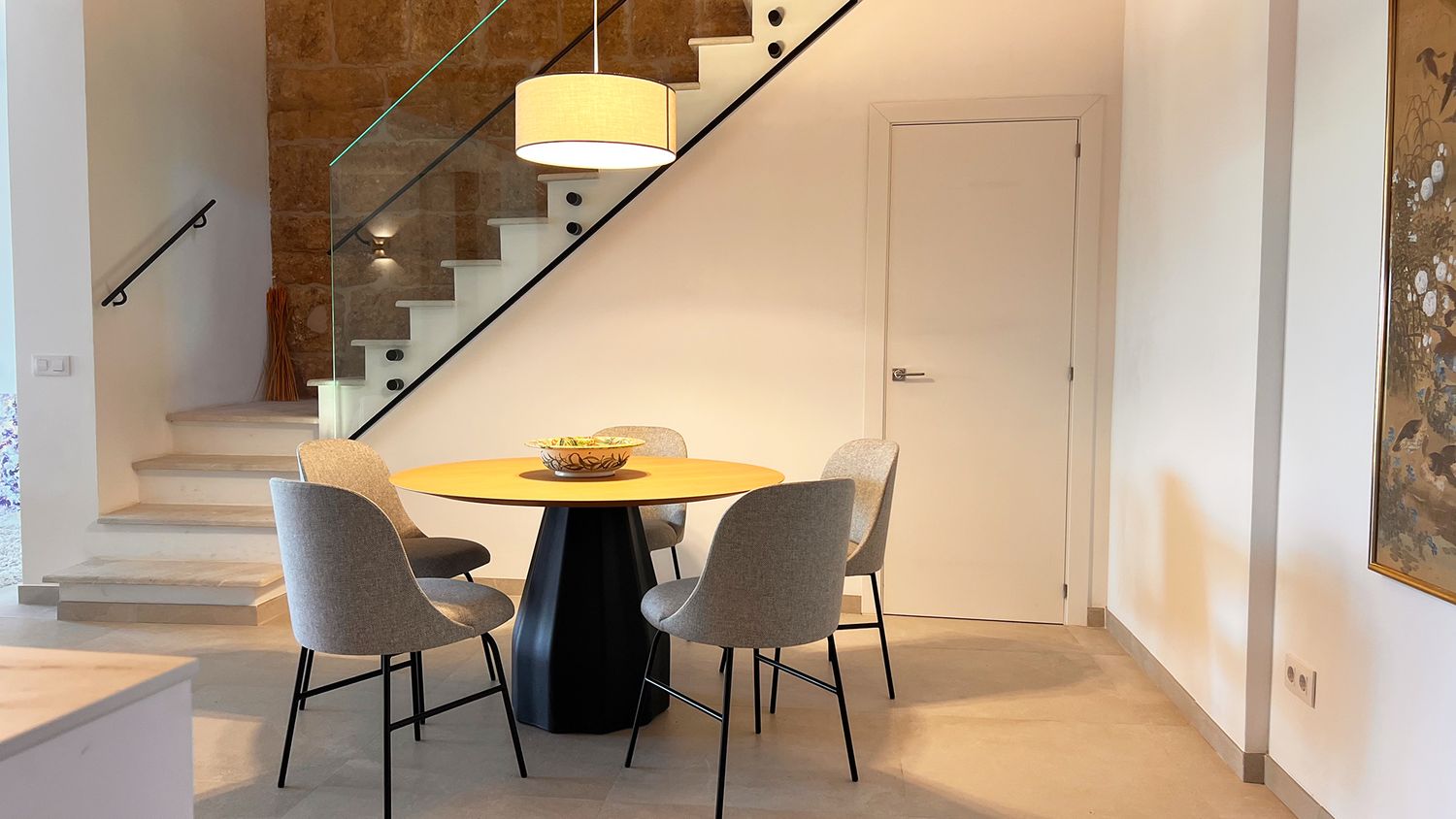 Round dining table with gray chairs positioned beneath a modern staircase.