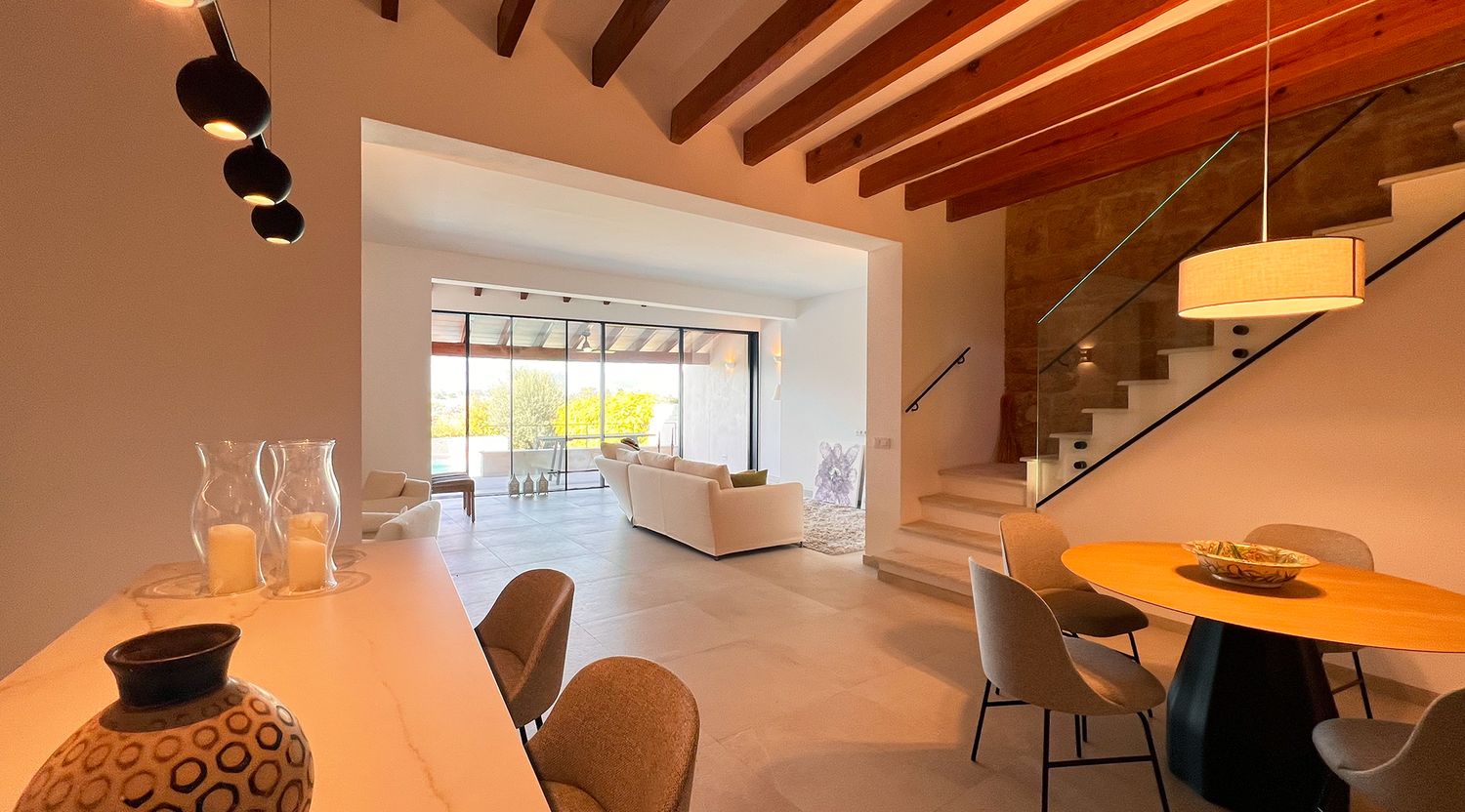 Open concept living space with wooden beams, glass staircase, and contemporary dining area.