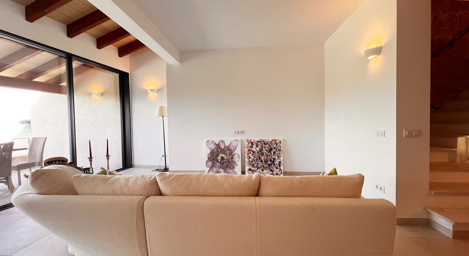 Bright living room with beamed ceiling, white sectional sofa and staircase.