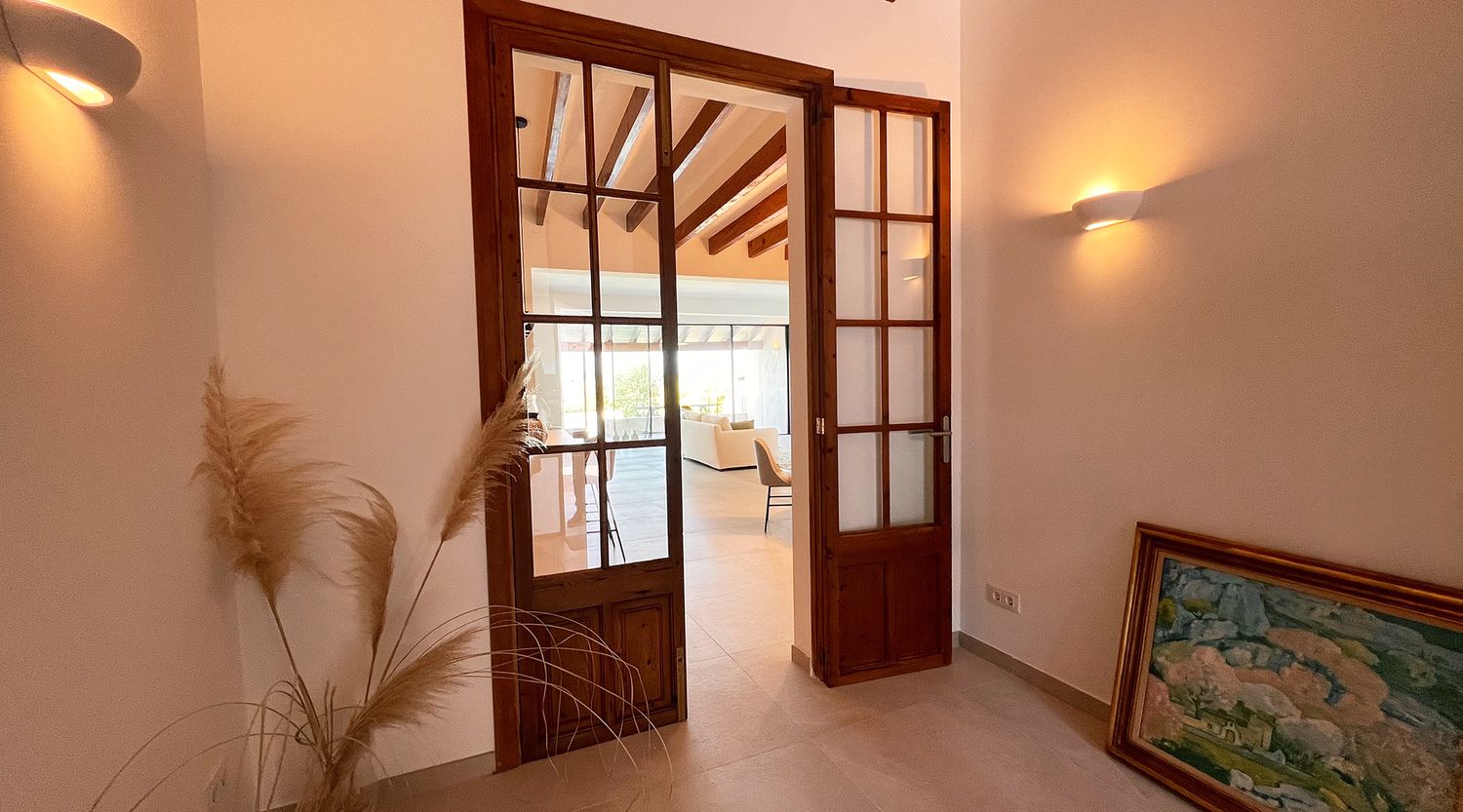 French doors with glass panels leading to living space with wooden ceiling beams and wall sconces.