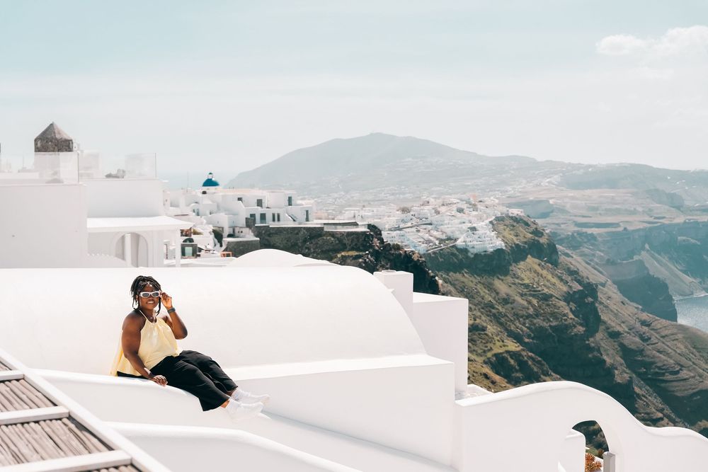 Person sitting on white rooftop in Santorini Greece with scenic caldera views and whitewashed buildings in background.