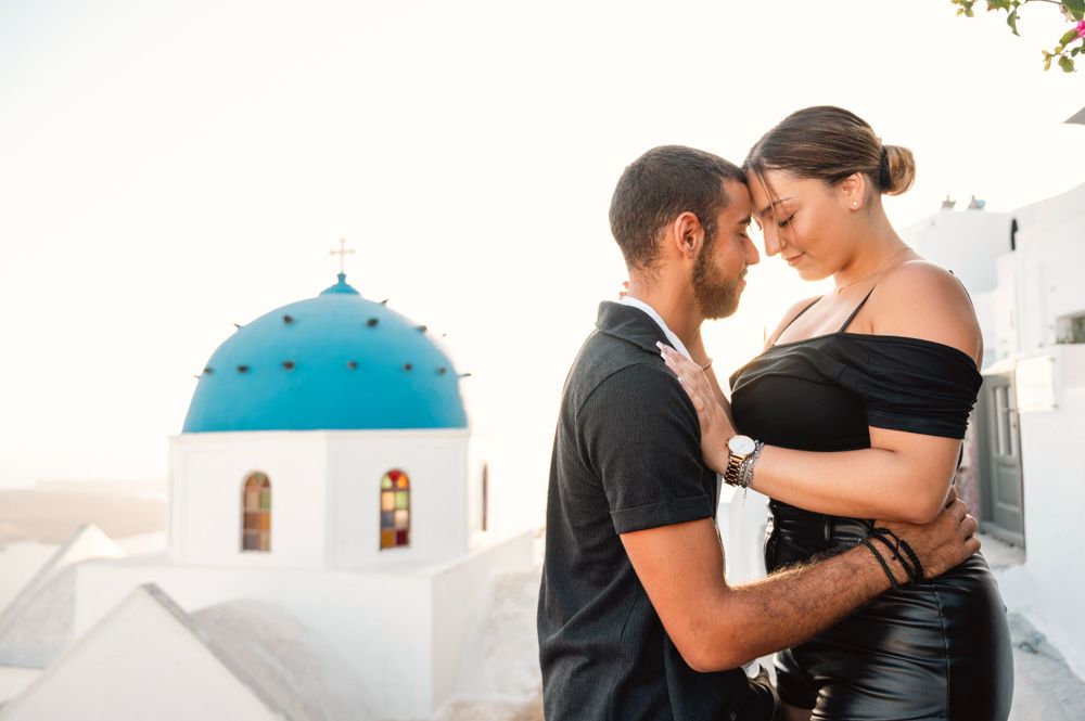 Romantic couple moment captured against iconic blue-domed church in Santorini.