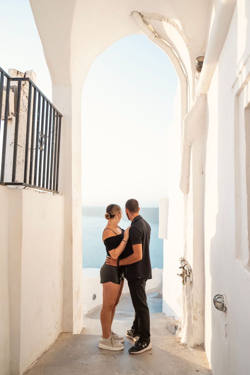 Intimate couple moment captured in white Mediterranean archway with ocean view.