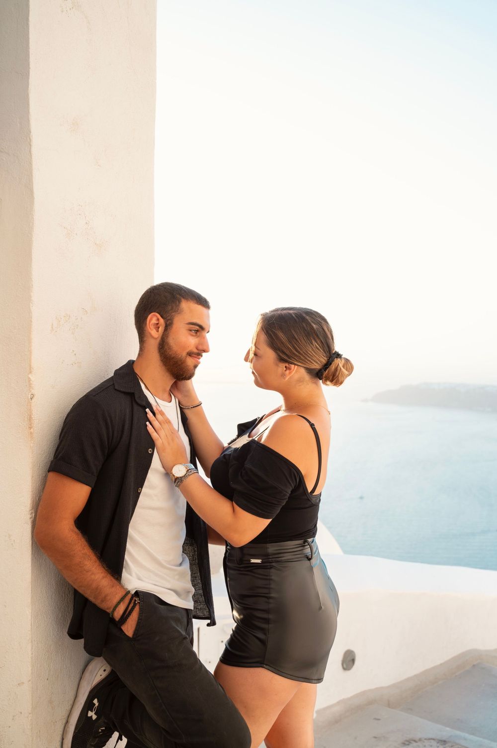 Romantic couple sharing an intimate moment against a white wall overlooking the Mediterranean Sea in Santorini.