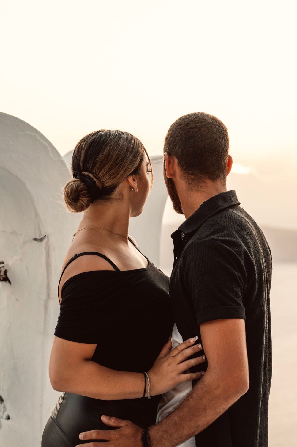Intimate moment between couple against white Mediterranean architecture at sunset.