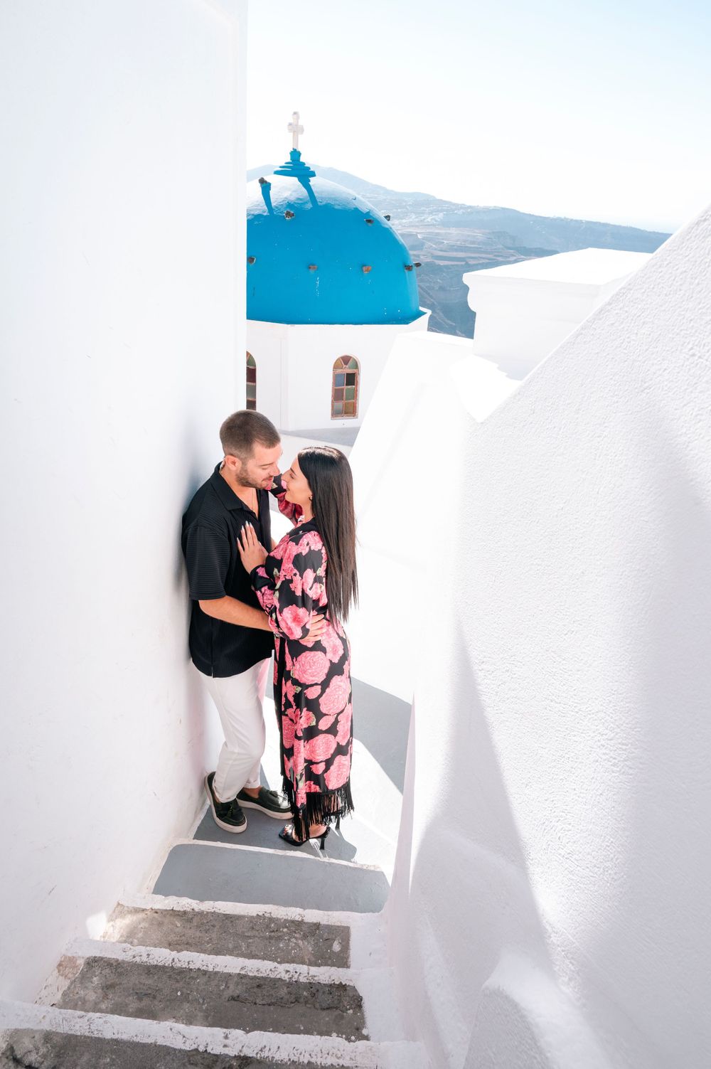 Romantic moment on traditional white steps of Santorini with blue dome church visible.