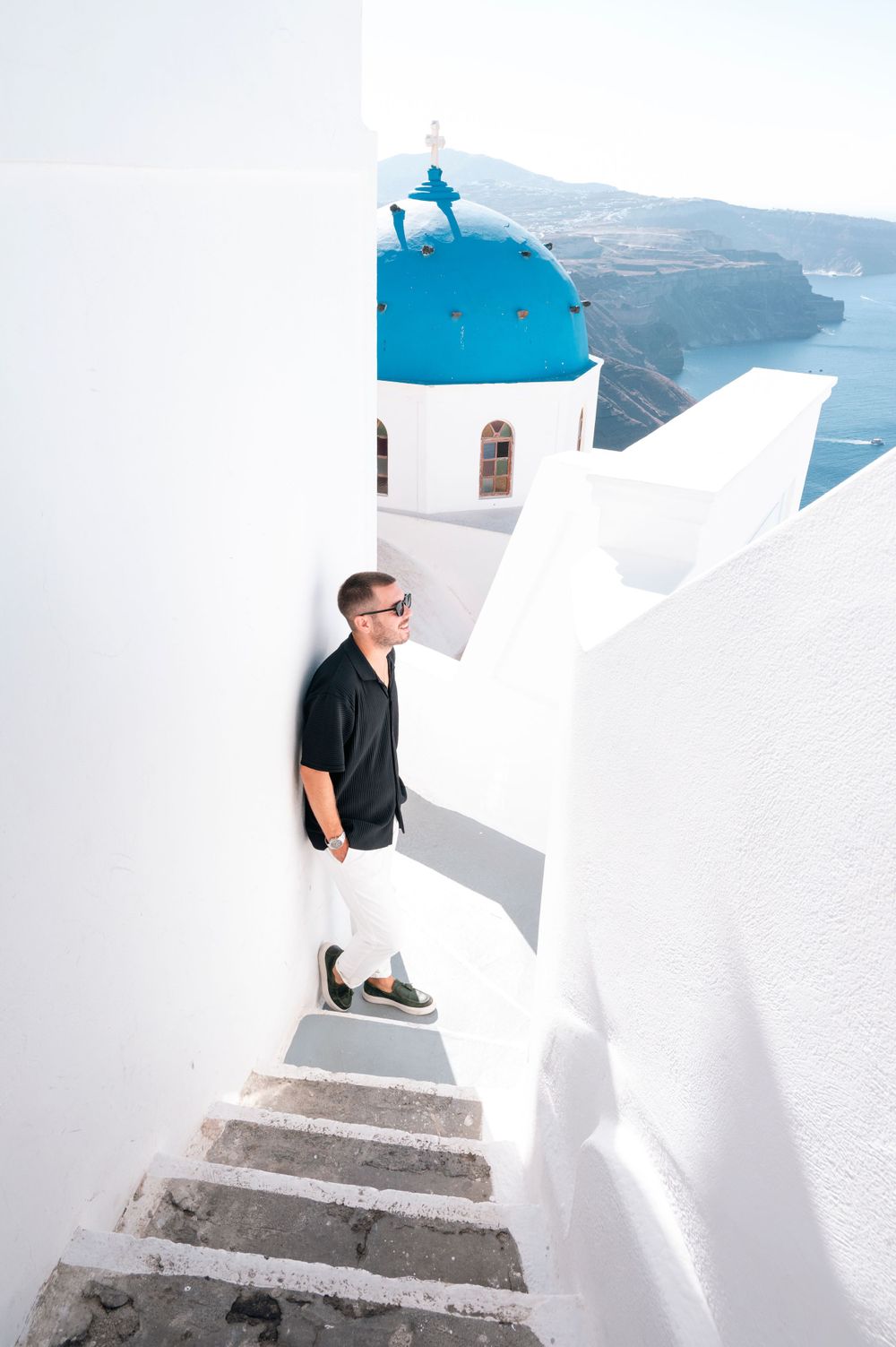 Person on white steps with classic Santorini blue dome church and sea view in background.
