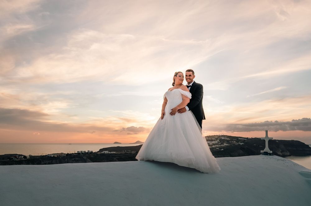 Bride and groom embracing at sunset on a white rooftop with scenic ocean views in Santorini, Greece.