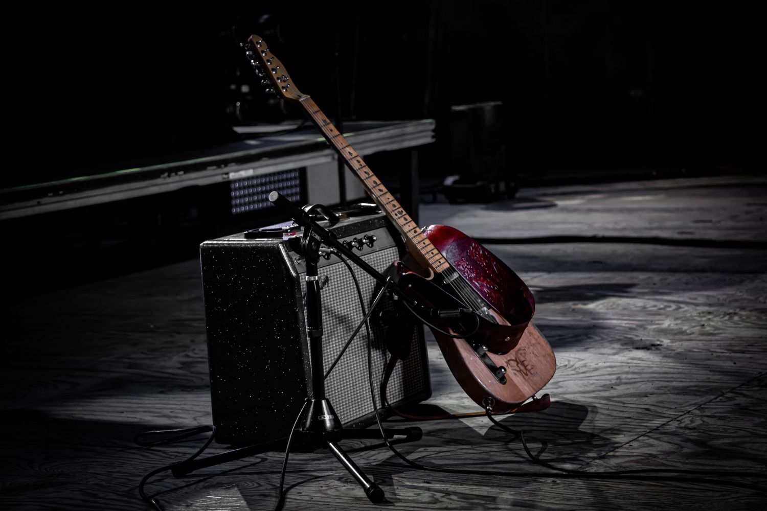 Electric guitar and amplifier on dark stage with dramatic spotlight.