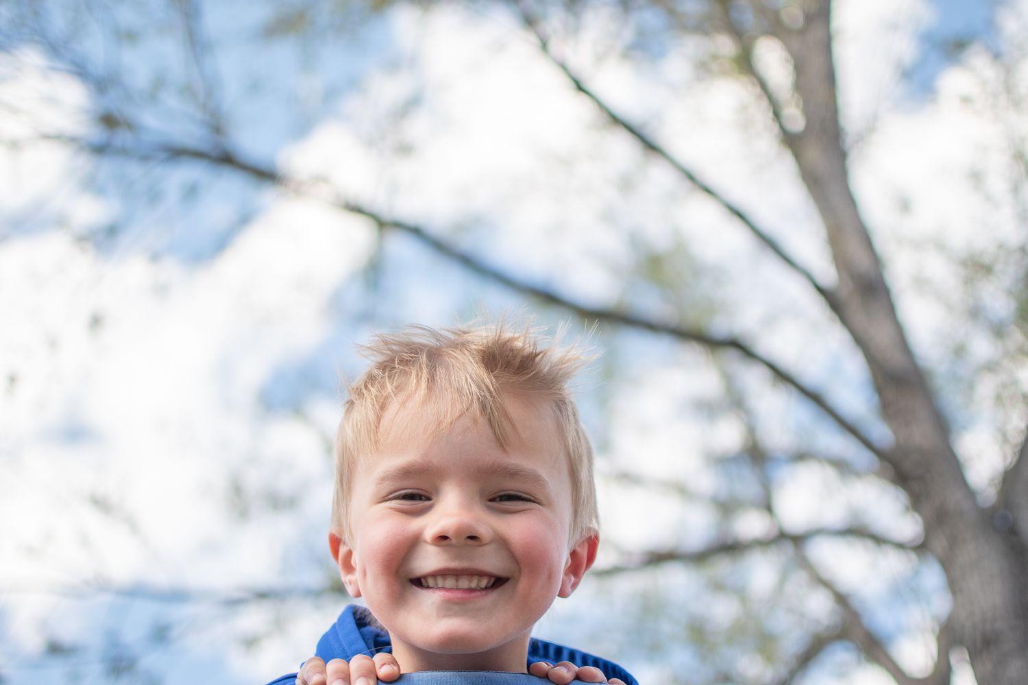 A joyful outdoor portrait against a bright blue sky with tree branches.