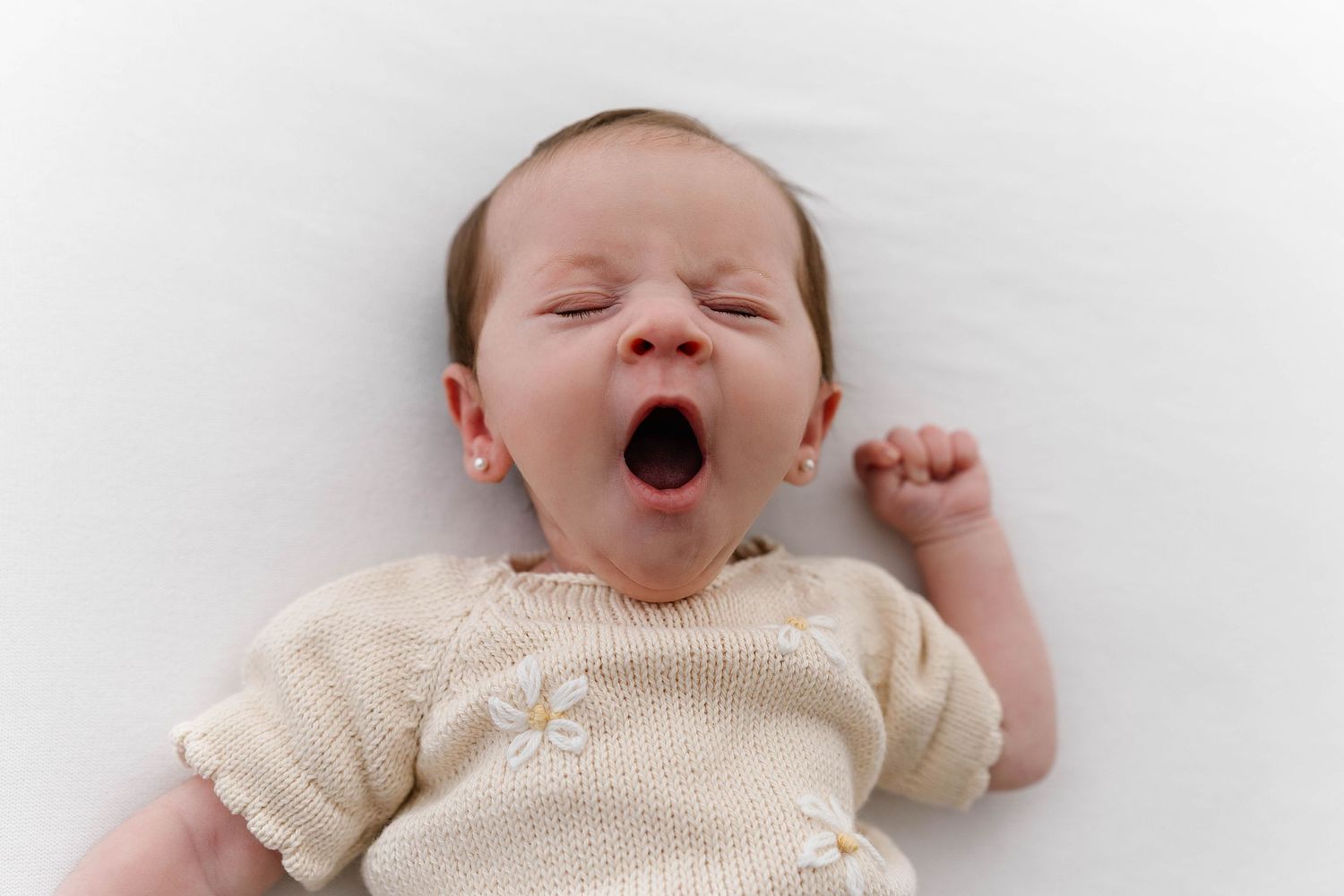 Yawning baby in cream knit outfit against white background.