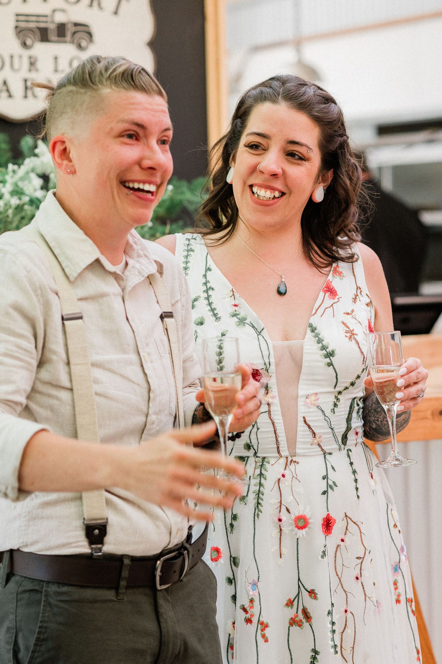 A couple shares a joyful laugh while holding champagne glasses at their wedding reception