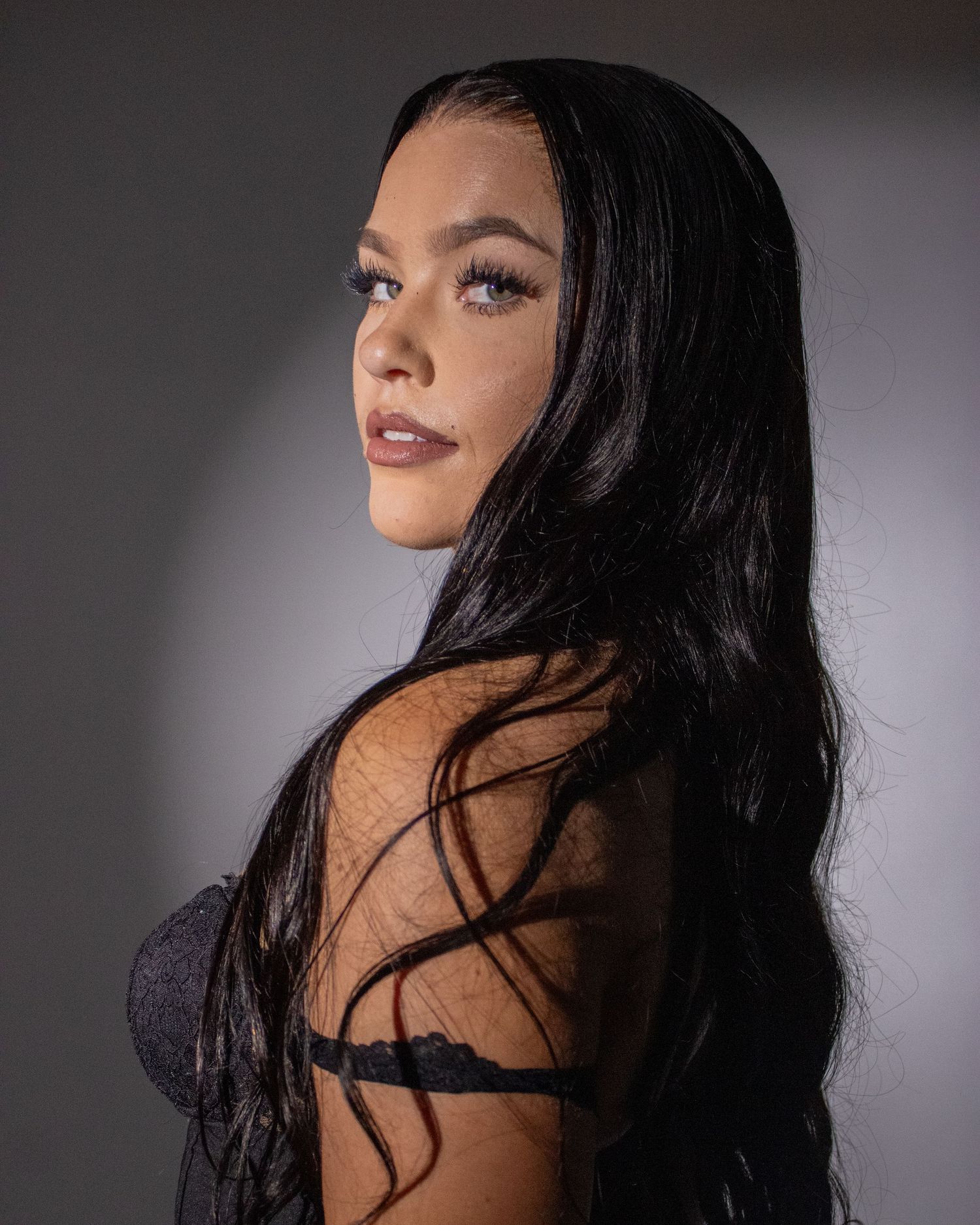 Woman with long black hair in black lingerie poses in dramatic studio lighting.