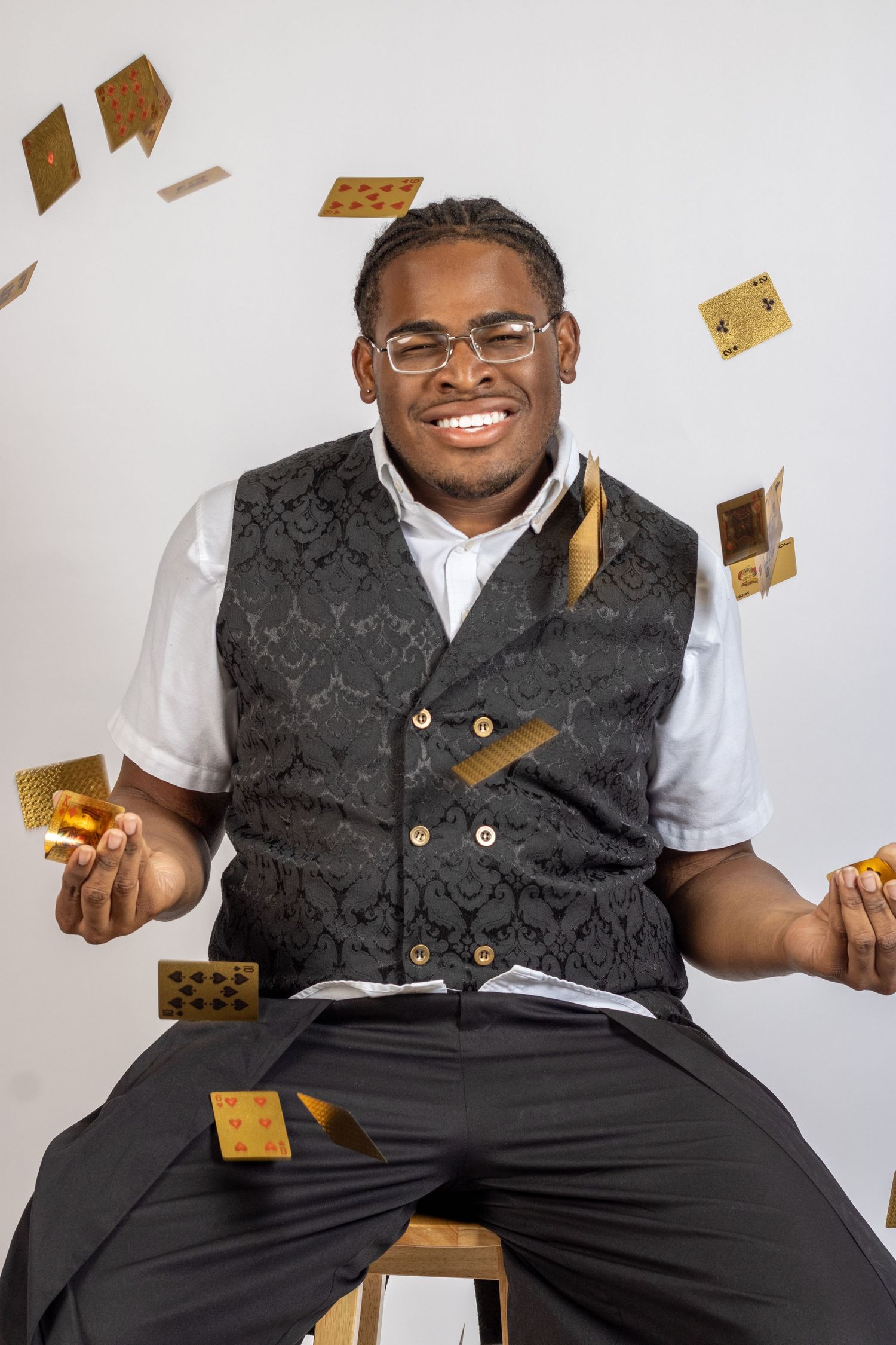 Graduate in formal attire smiles while surrounded by floating golden graduation caps.