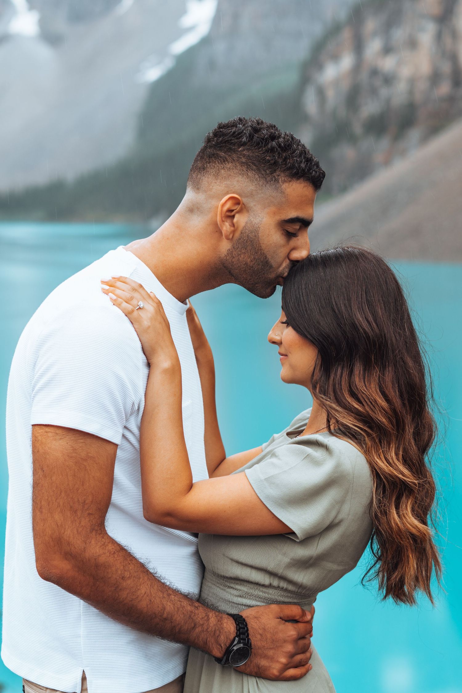 Groom kisses the bride's forehead by Moraine Lake. Banff engagement photography.