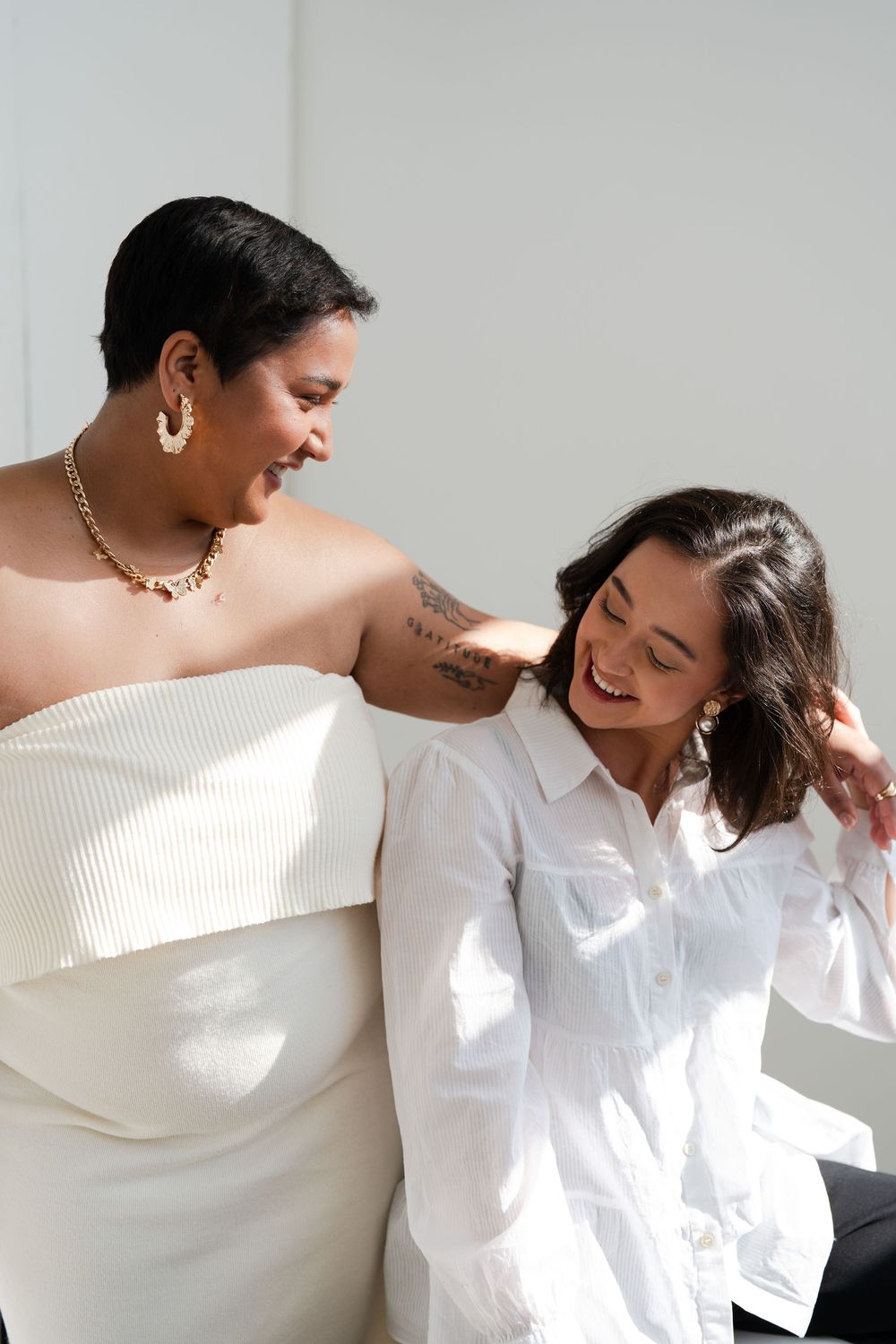 Two people share a joyful candid moment together while wearing white against a neutral background.