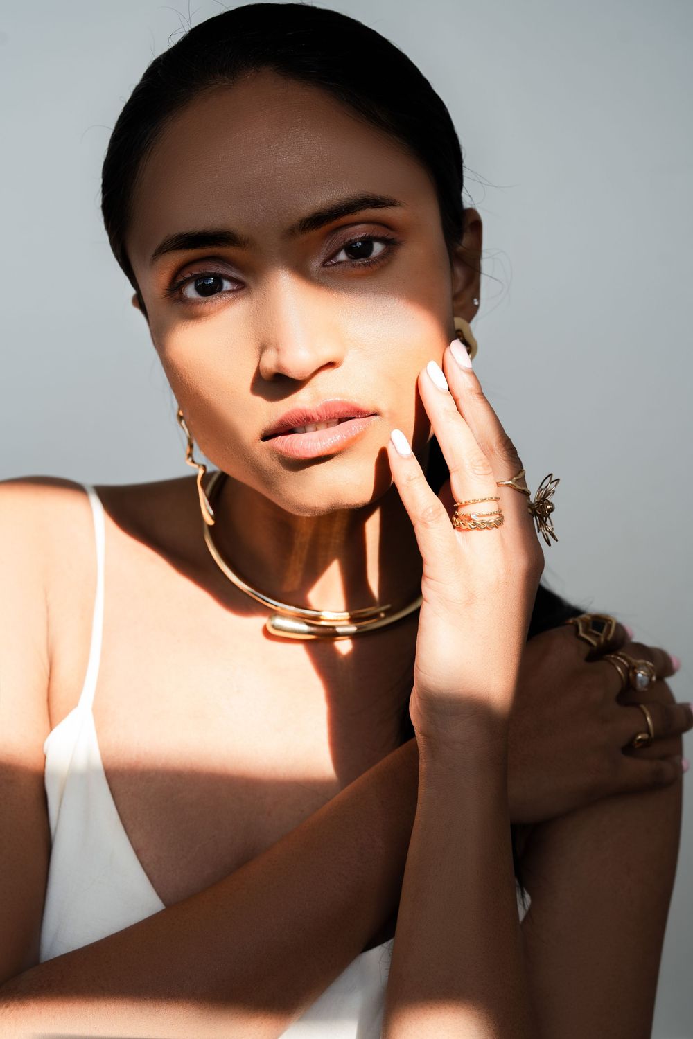 Glamorous photo with dramatic lighting showcasing a model wearing gold jewelry and casting striking shadows on their face.