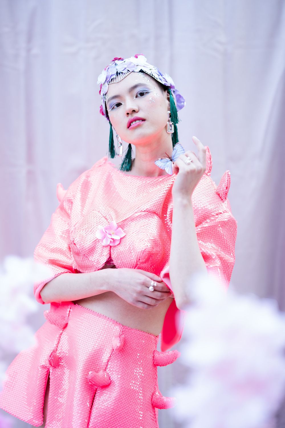 Fashion portrait featuring pink textured dress with floral headpiece and teal tassel earrings.