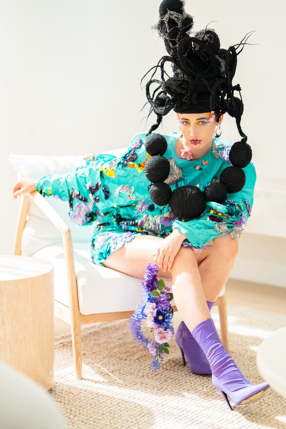 Avant-garde fashion featuring turquoise outfit and elaborate black pom-pom headpiece.