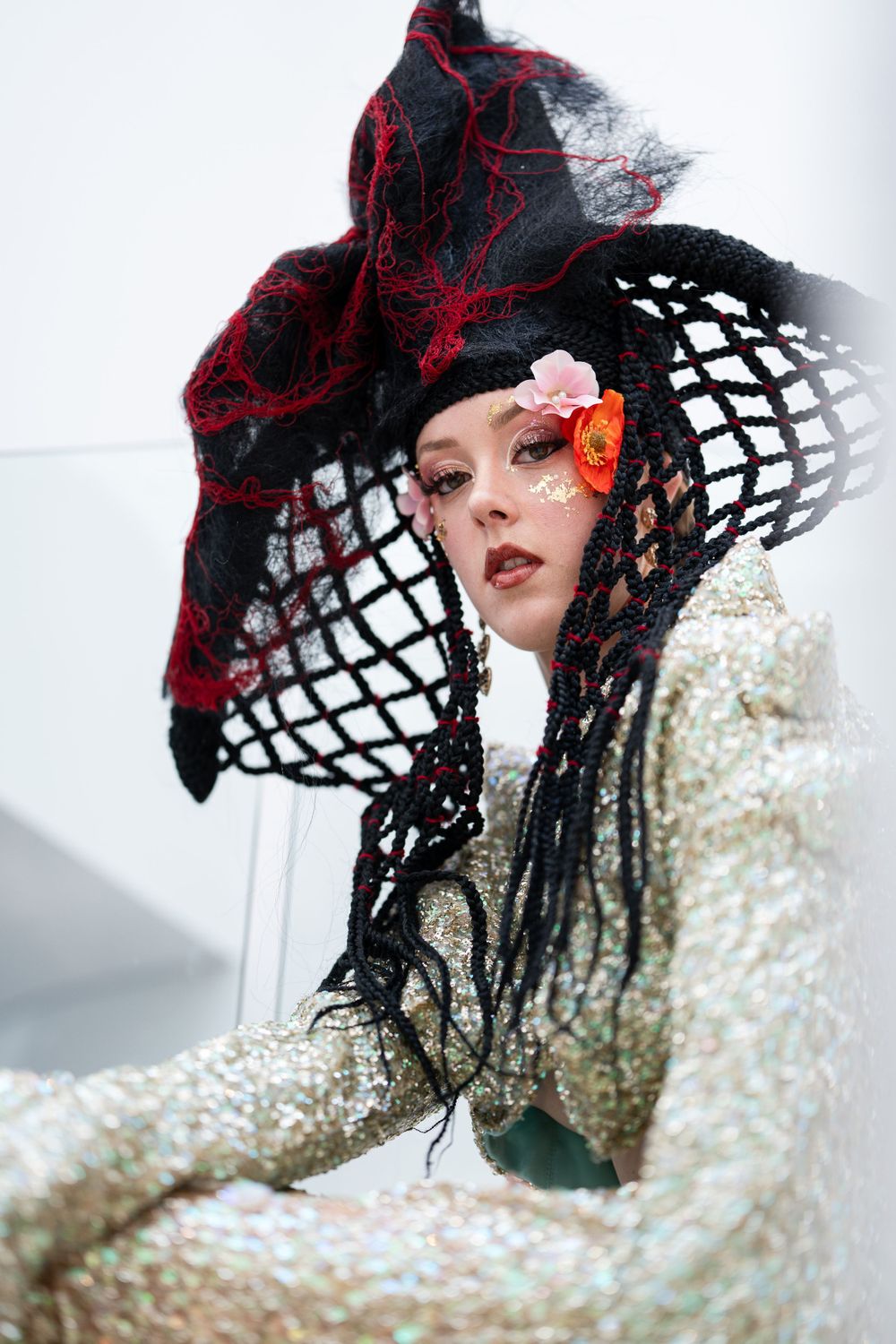 Gothic fashion portrait with dramatic red and black mesh hat against white background.