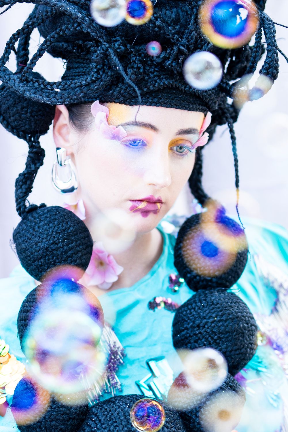 Artistic portrait with black sculptural headpiece, bubble effects, and blue eye makeup.