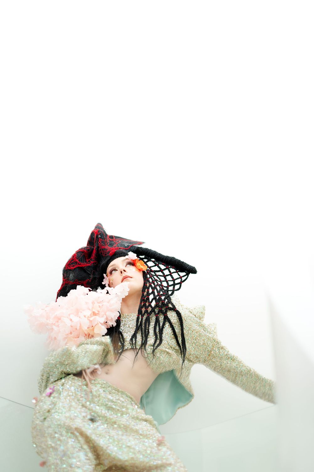 High fashion portrait with black netted headpiece and pink cotton candy elements against white background.