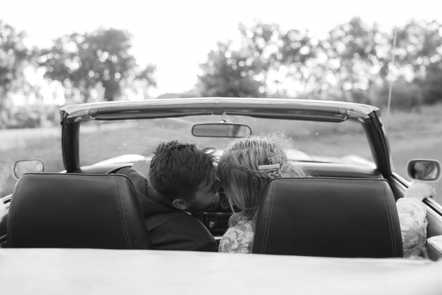 Black and white photo of couple sharing an intimate moment in a convertible car.