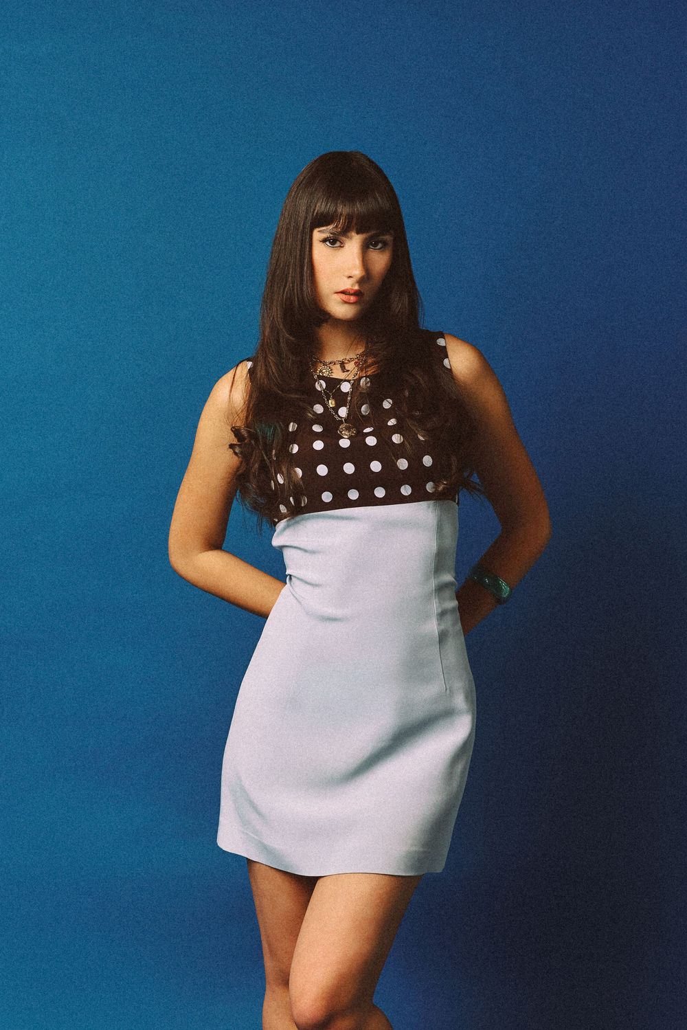 Young woman in retro polka dot mini dress posing against blue background.