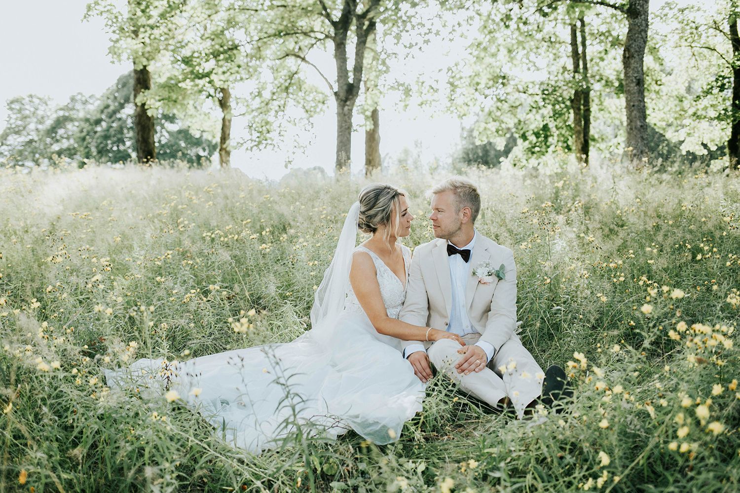 Malin och Olas bröllopsporträtt vid Kvarntorps Herrgård.  Bröllopsfotograf i Karlstad Rebecca Nordin. Brudparet sittande på ängen.