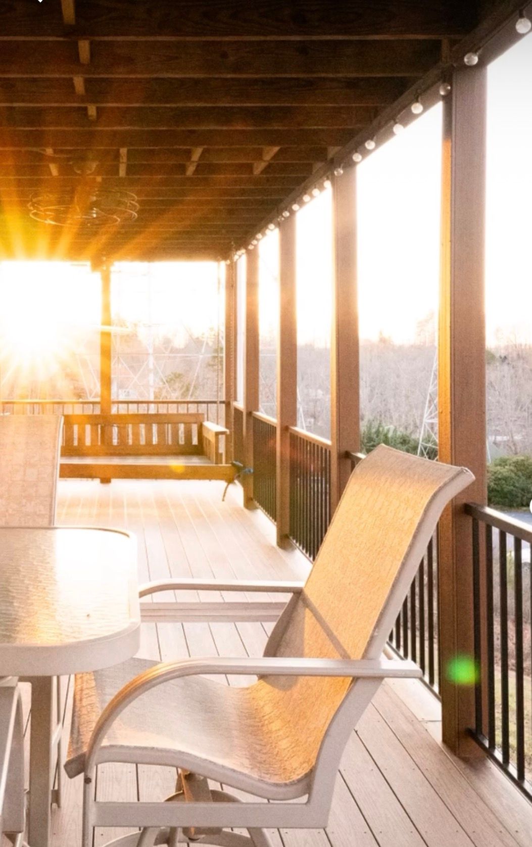 White patio chairs on a covered deck at sunset with golden sunlight streaming through the wooden railings.