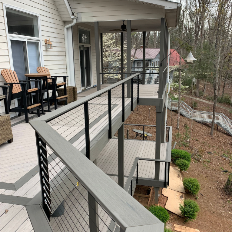 Modern deck with black cable railing system and Adirondack chairs overlooking a wooded backyard area.