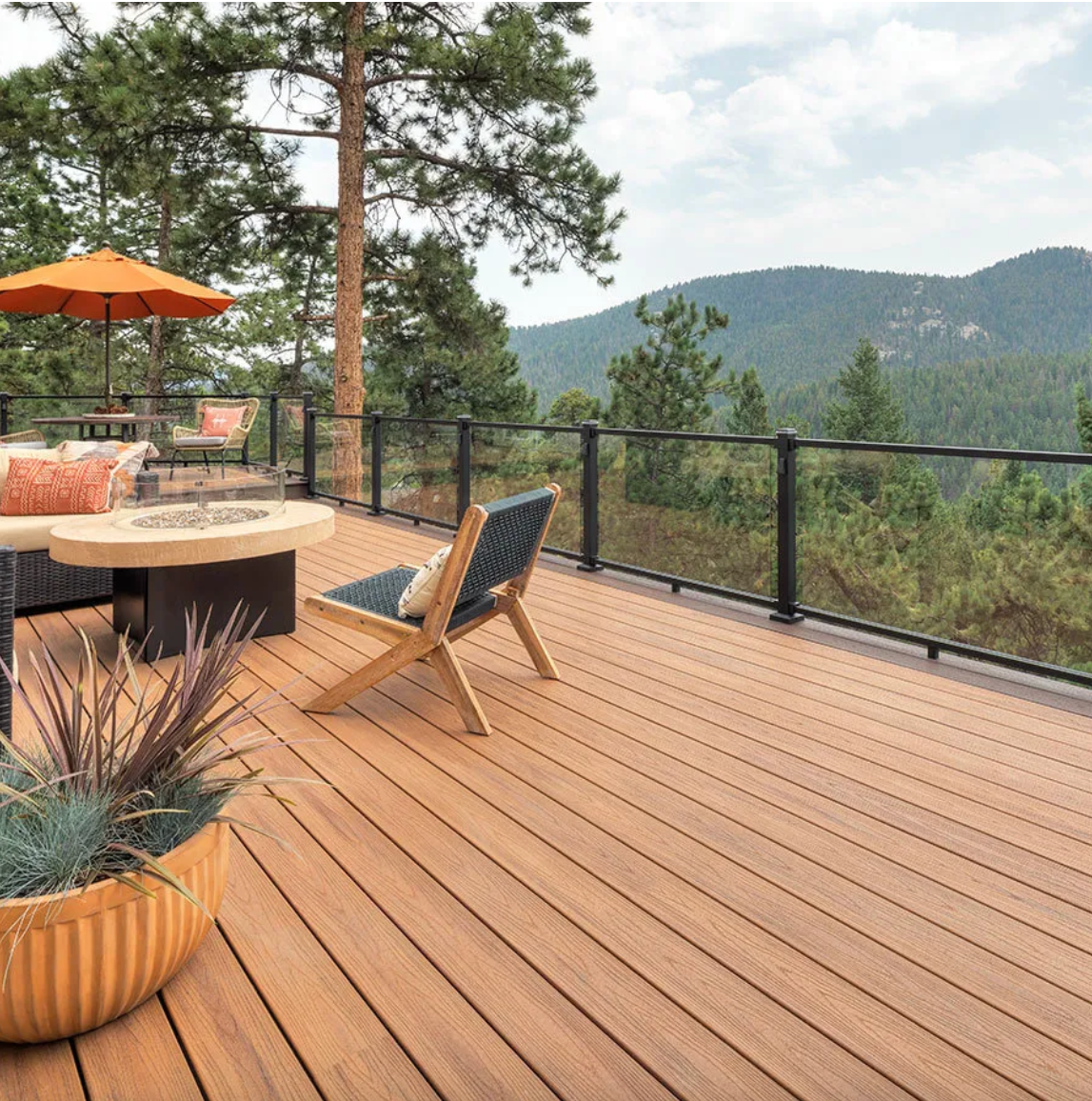 Spacious wooden deck with mountain views features modern outdoor furniture and orange patio umbrella in natural setting.