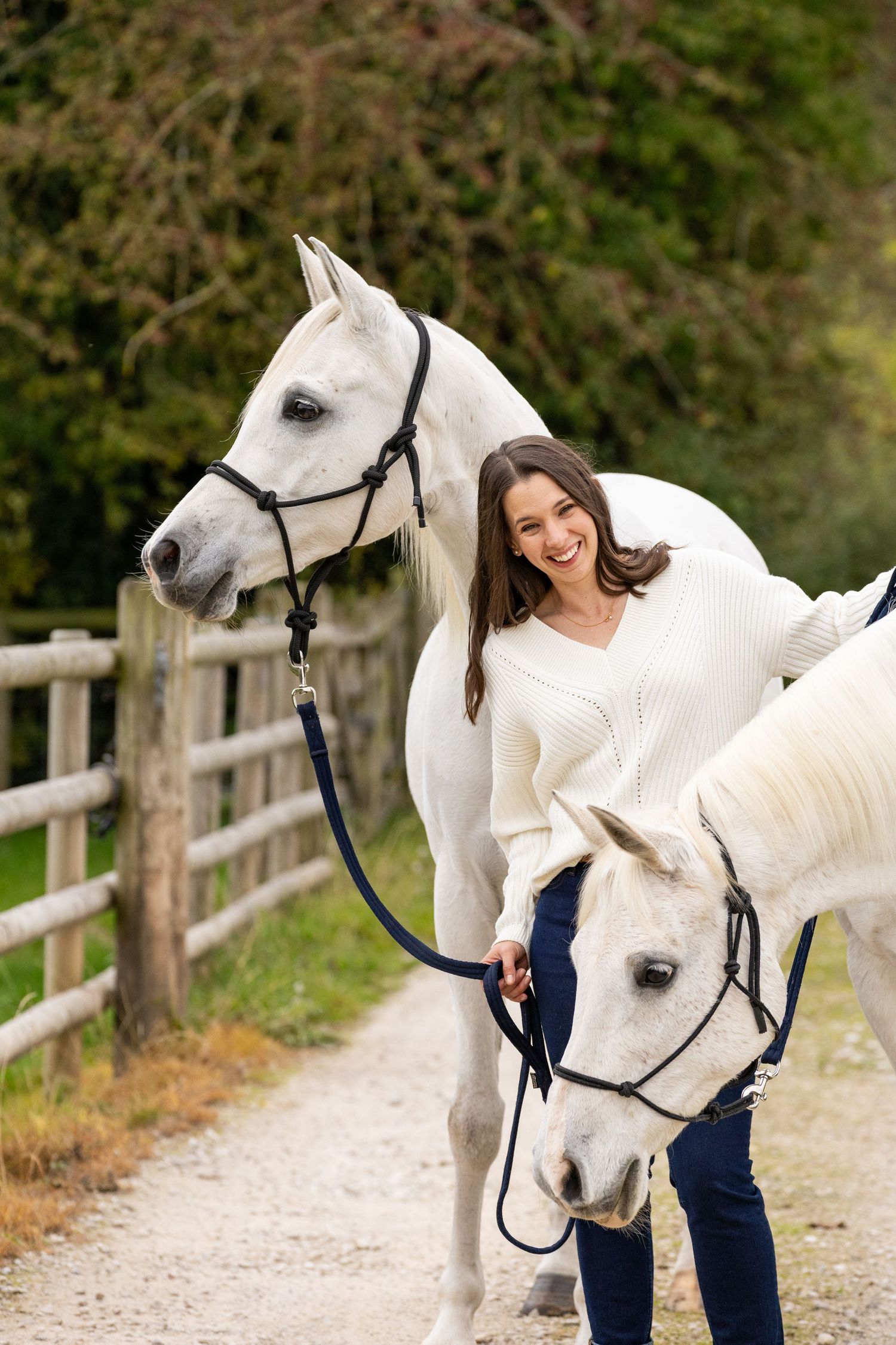 A brown horse and person in a tan jacket stand together in a wooded autumn setting.