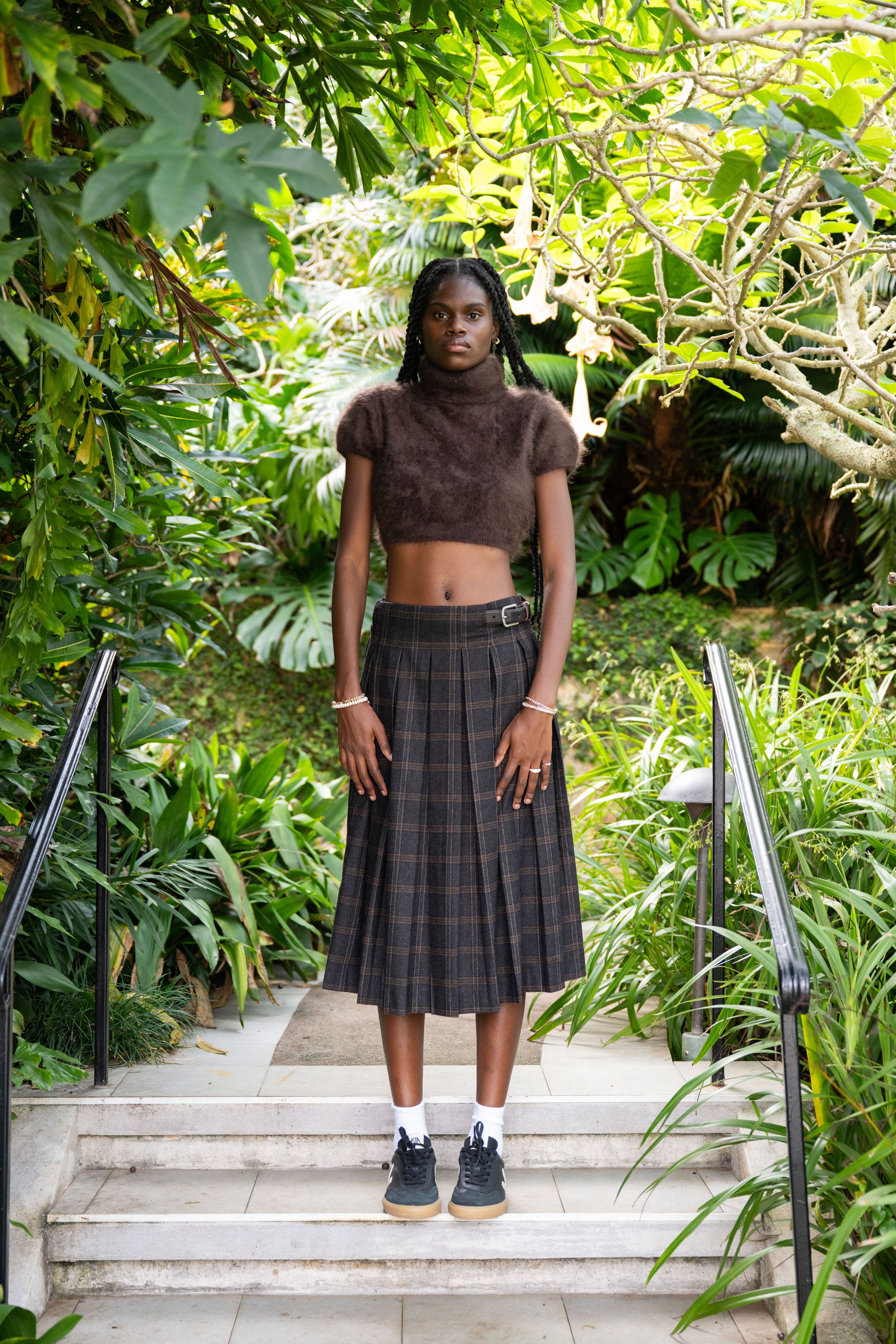 A series of photos showing someone wearing a plaid pleated skirt and brown top posing on outdoor concrete steps.