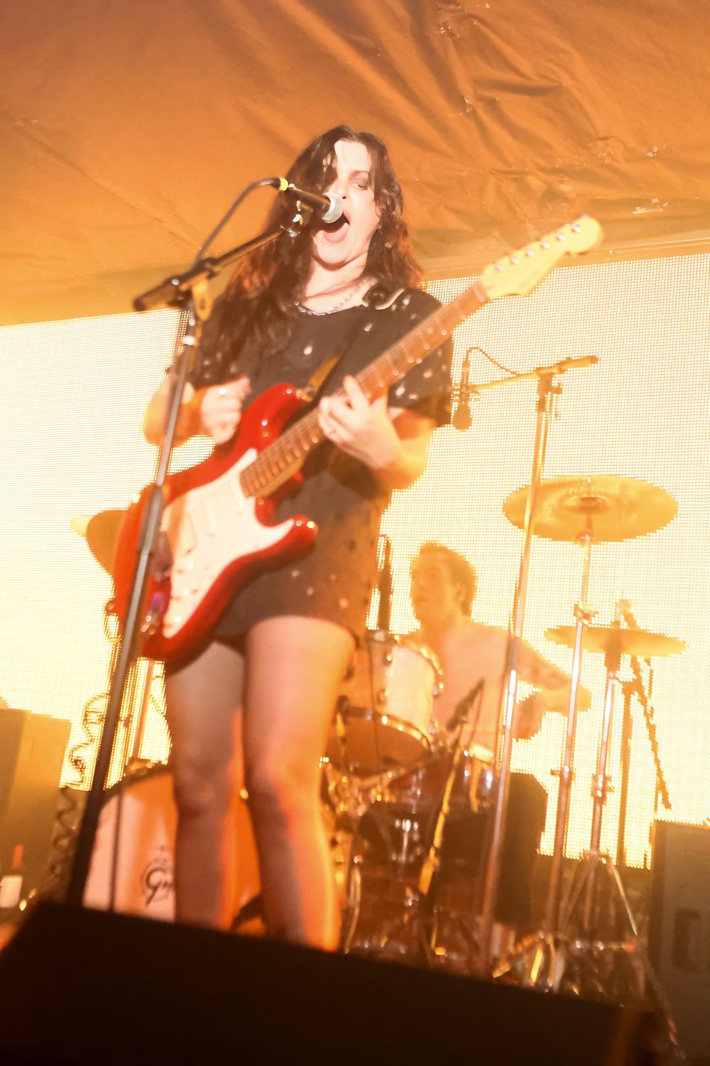 Musician performs on stage with electric guitar bathed in warm orange lighting during live concert performance.