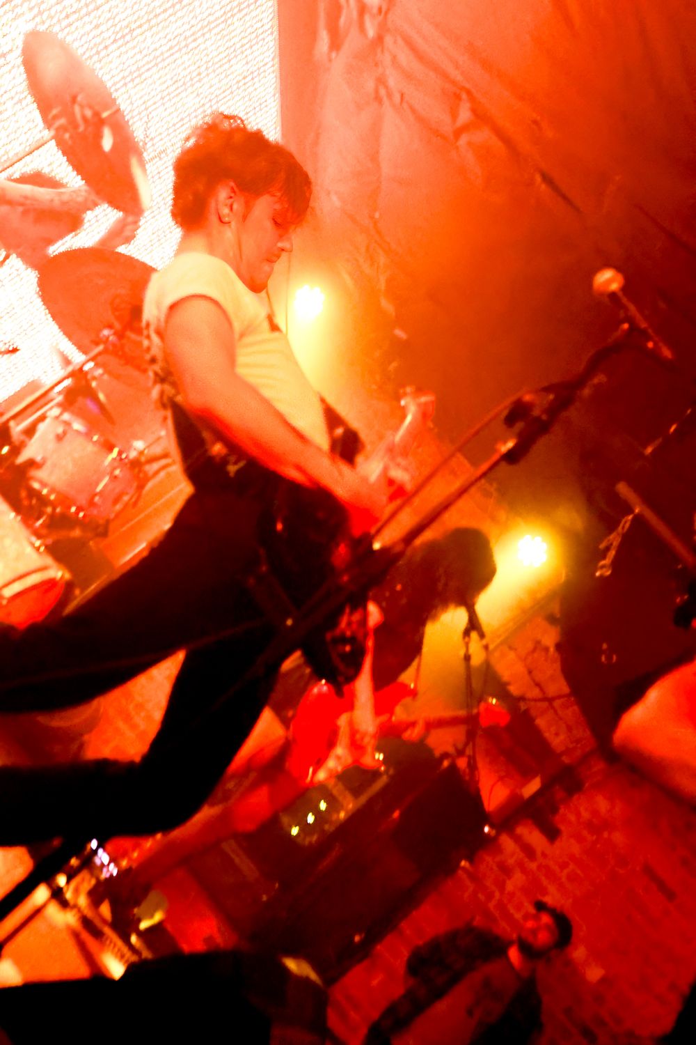 Rock band performs on dimly lit stage with dramatic red lighting creating moody atmospheric effect.