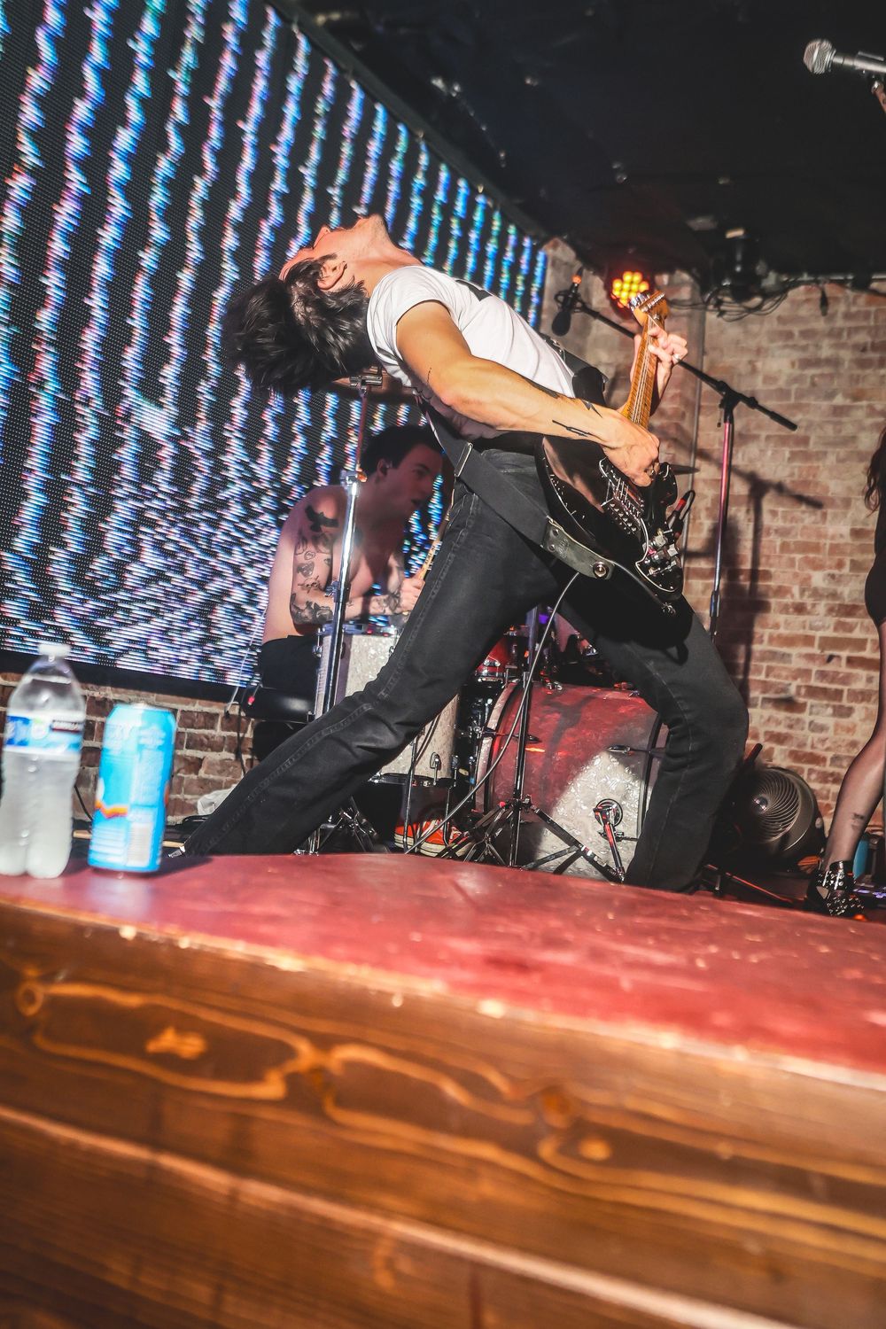 A sequence of photos showing a performer jumping over a wooden bar at a live music venue with brick walls and stage lighting.