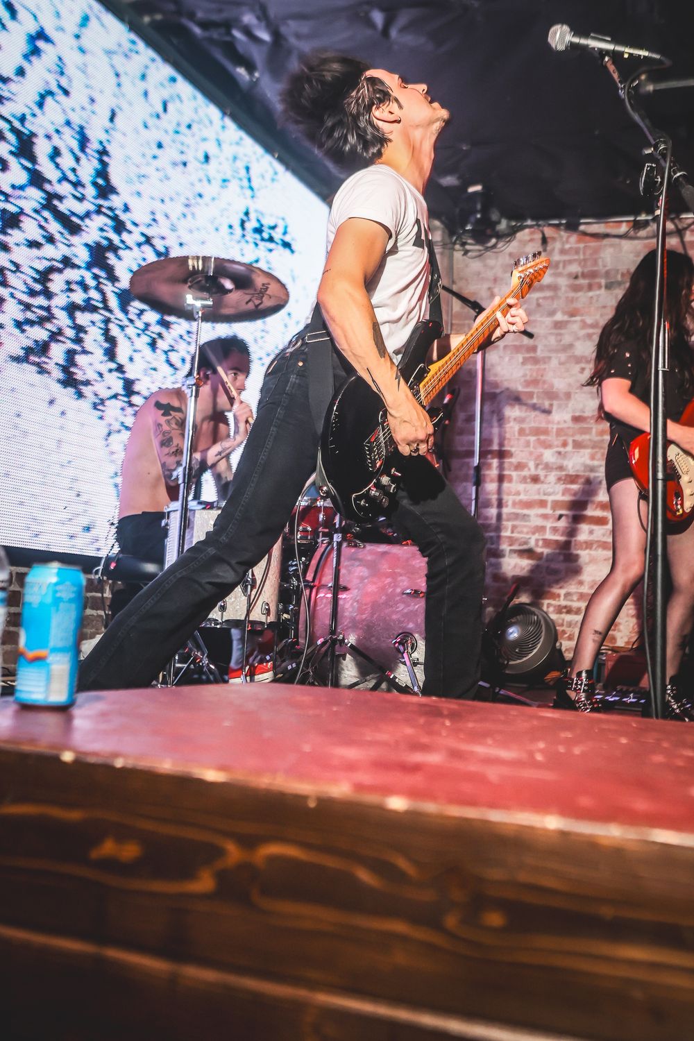 Rock band performs energetically on stage with brick wall backdrop and dramatic blue lighting effects.