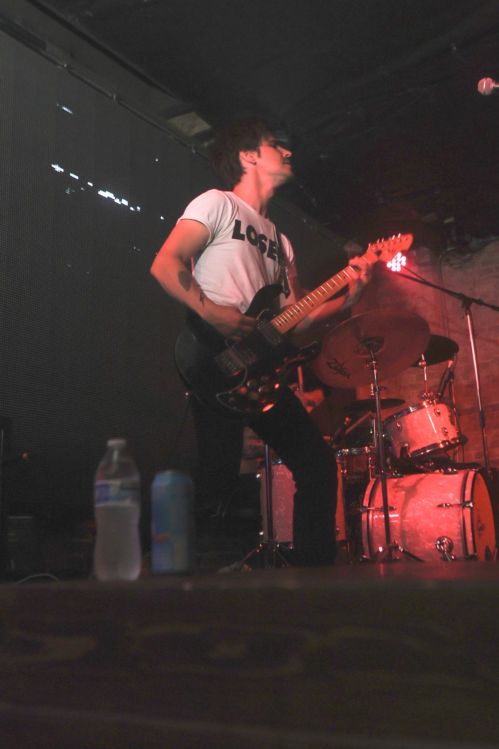 Musicians perform on a dimly lit stage with red lighting creating a moody rock concert atmosphere.