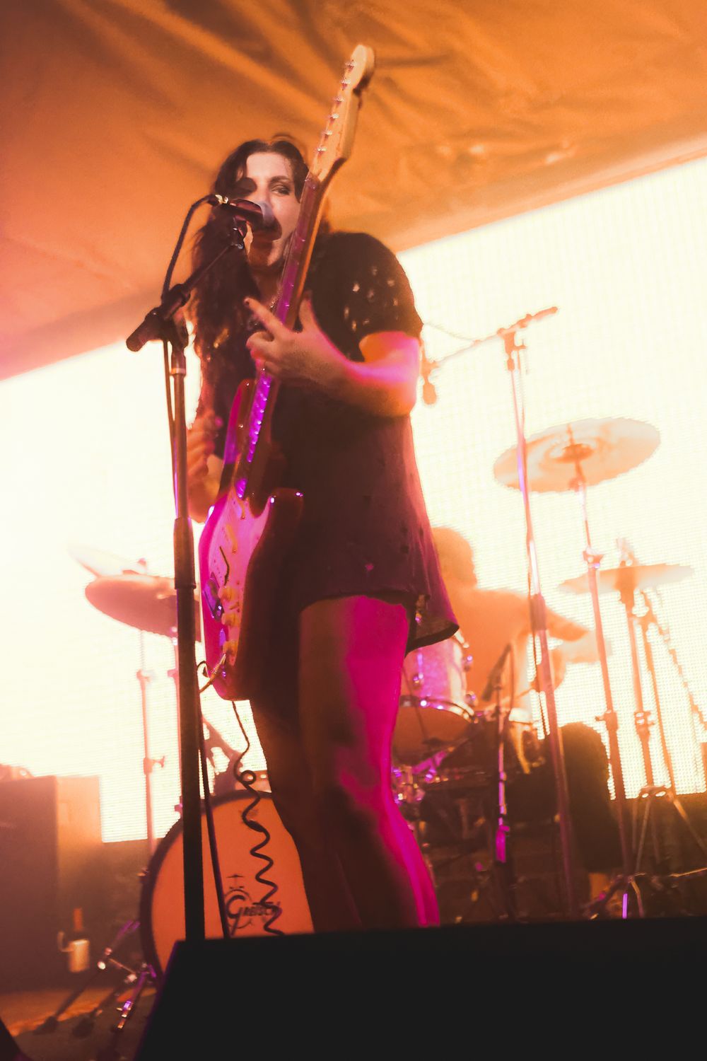 Concert performers silhouetted on stage with dramatic orange and pink lighting during a live music performance.