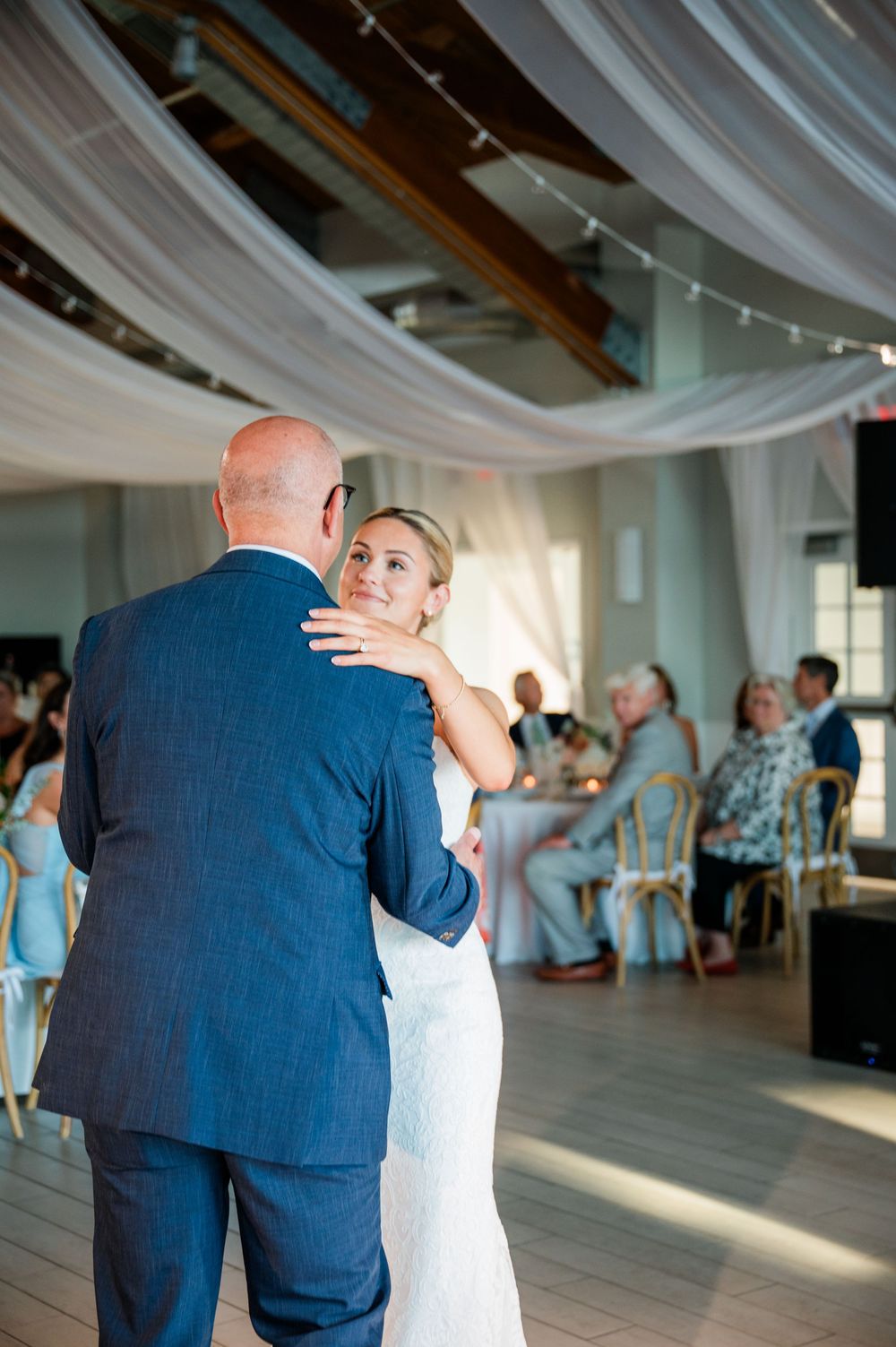 A couple shares an intimate dance moment at their wedding reception under elegant white draping.
