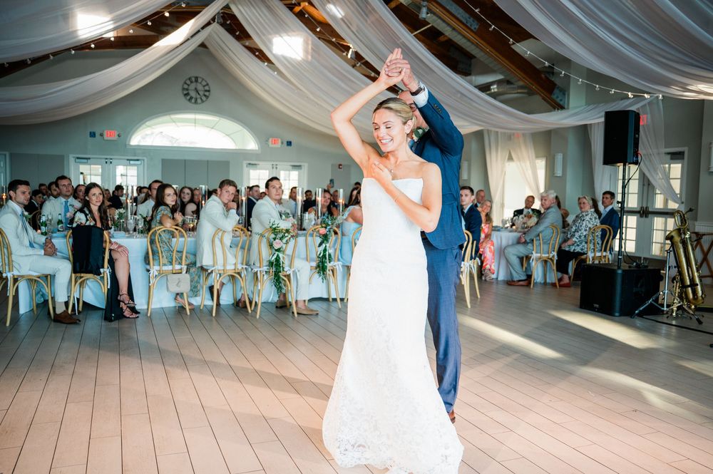 Wedding guests dancing and celebrating on a white dance floor at an indoor reception venue.