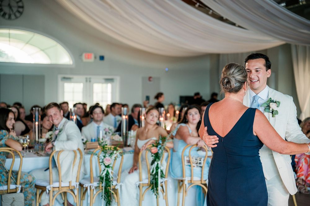 Wedding guests dancing together in an elegant reception hall with white draped ceiling and gold chairs.