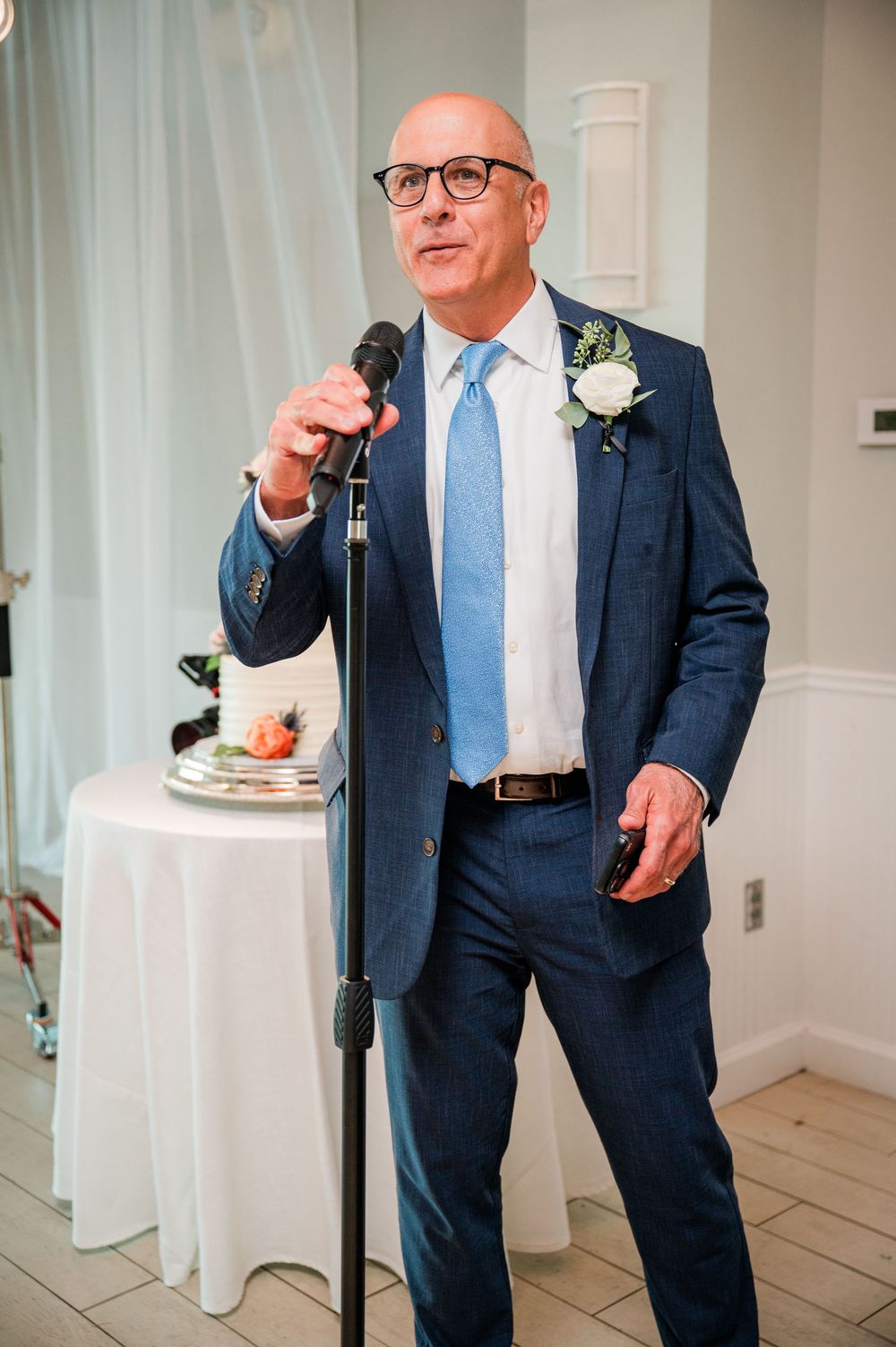 A gentleman in a navy suit and blue tie enjoys refreshments at an elegant indoor event.