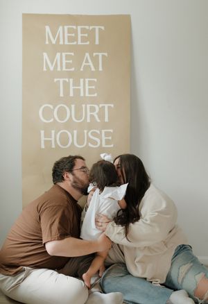 A couple poses intimately in front of a sign reading 'Meet Me At The Court House'.