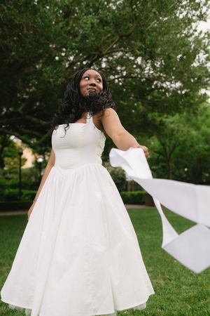 A person in a flowing white dress twirls joyfully on green grass in an outdoor setting.