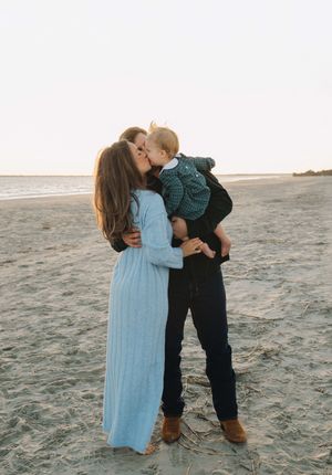 Tender family moment captured in silhouette on a sandy beach at dusk.