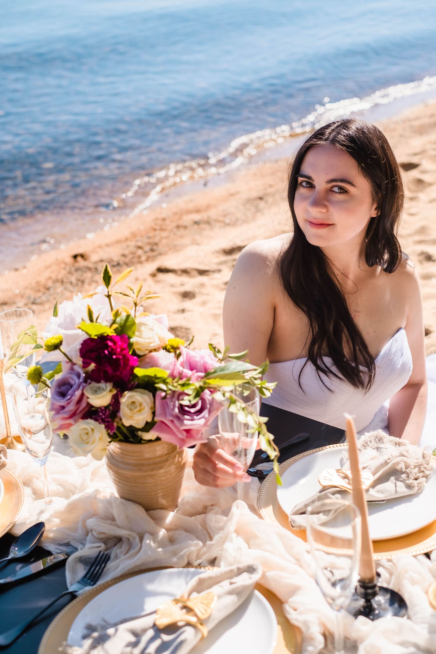 Romantic beachside picnic setup with colorful floral arrangement and elegant place settings along the shore of lake Tahoe California.